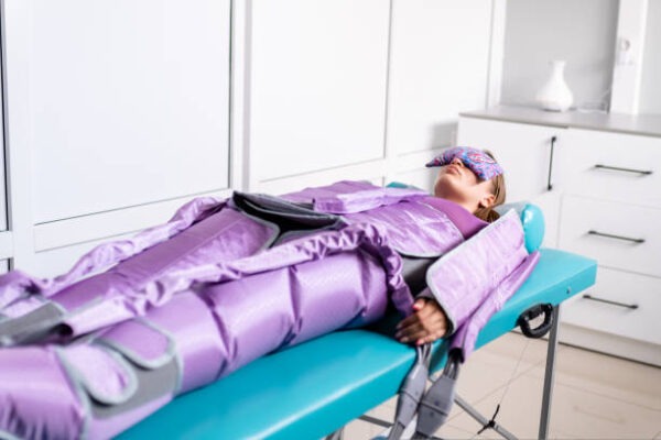 Woman lying with closed eyes during pressotherapy session in beauty clinic.